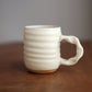 Cream ceramic mug with a handle on a wooden surface and gray background