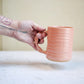 Person holding a pink ceramic mug with a neutral background