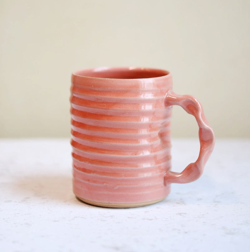 Pink ceramic mug on a white surface with a neutral background