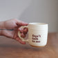 Hand holding a cream handmade ceramic mug with 'Don't talk to me' text on a wooden surface.