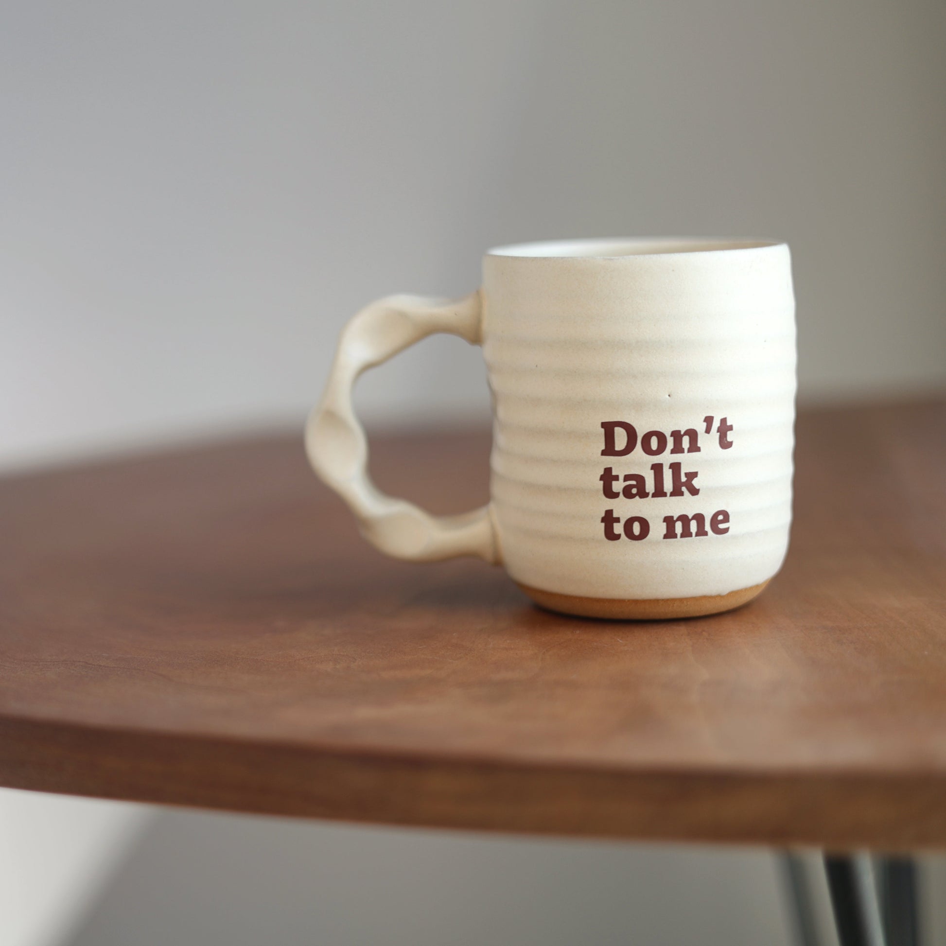 Off White handmade companion mug with 'Don't talk to me' text on a wooden table against a plain background