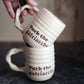 Two stacked ceramic mugs with 'Fuck the patriarchy' text on a dark surface.