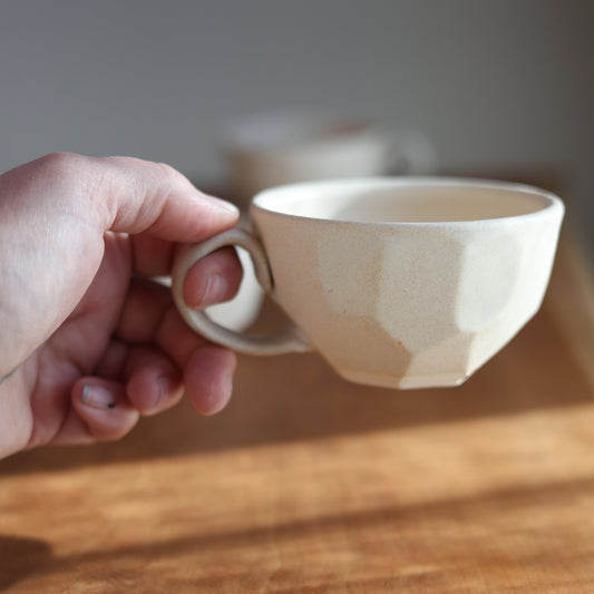 Hand holding a faceted ceramic cup on a wooden surface with a blurred background