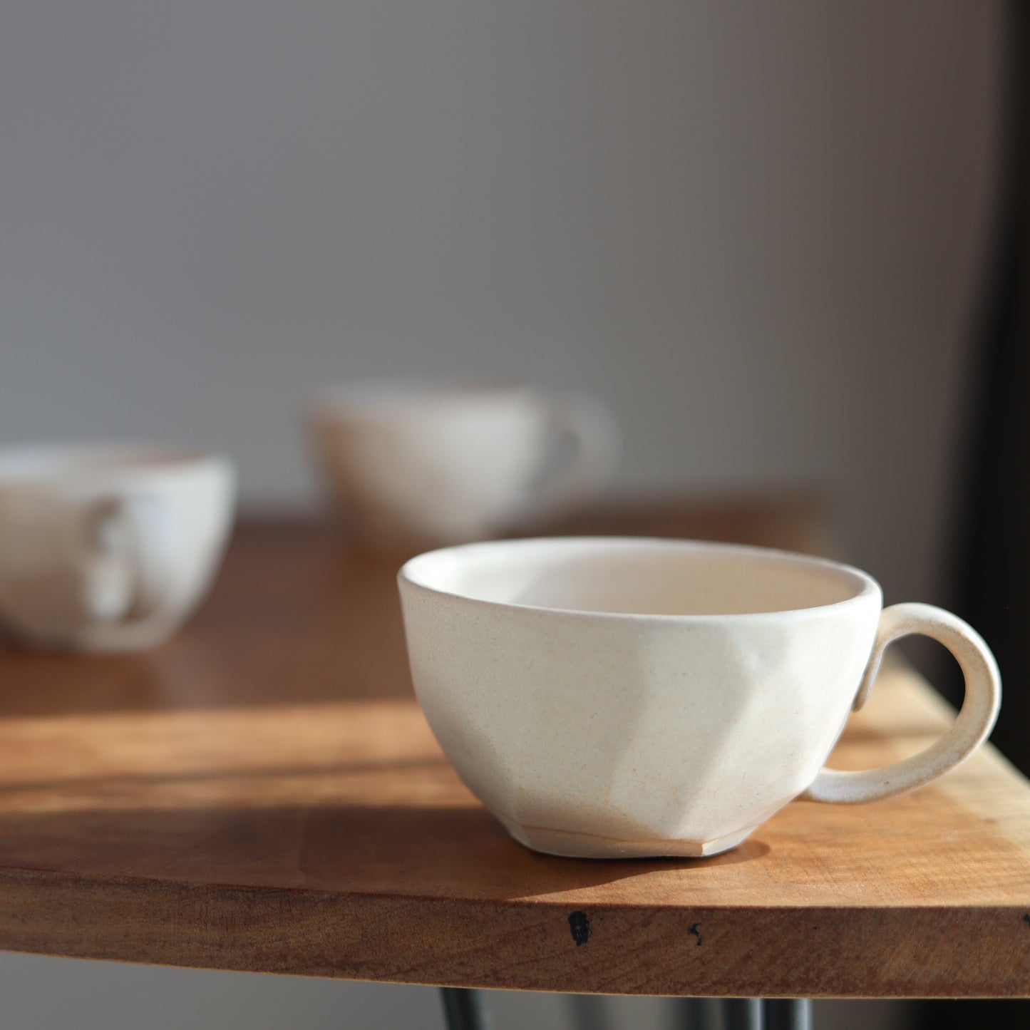White ceramic faceted tea cups on a wooden table with a blurred background