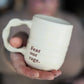 Person holding a mug with 'Fear our rage.' text, blurred background