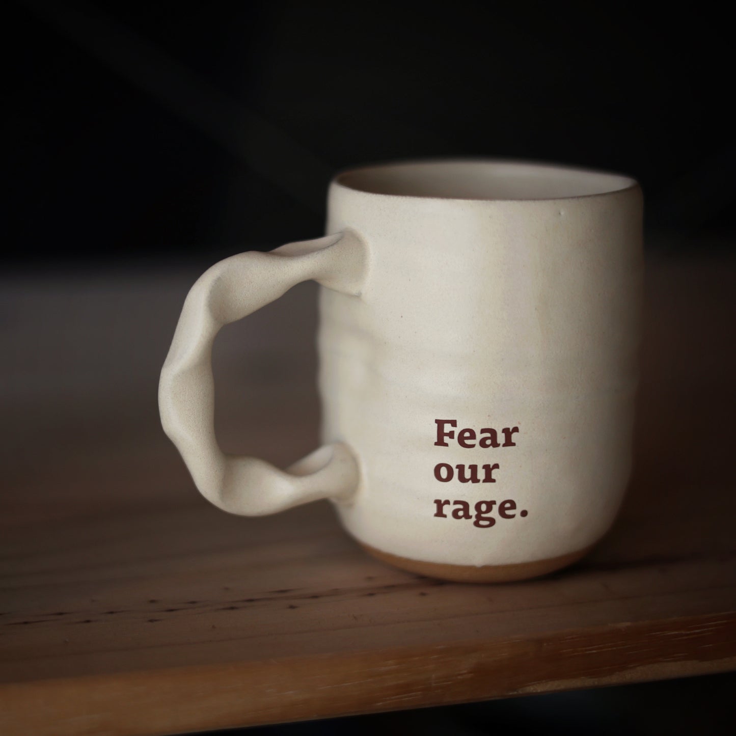 White mug with 'Fear our rage' text on a wooden surface