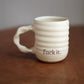 Cream ceramic mug with 'fuck it.' text on a wooden surface and gray background