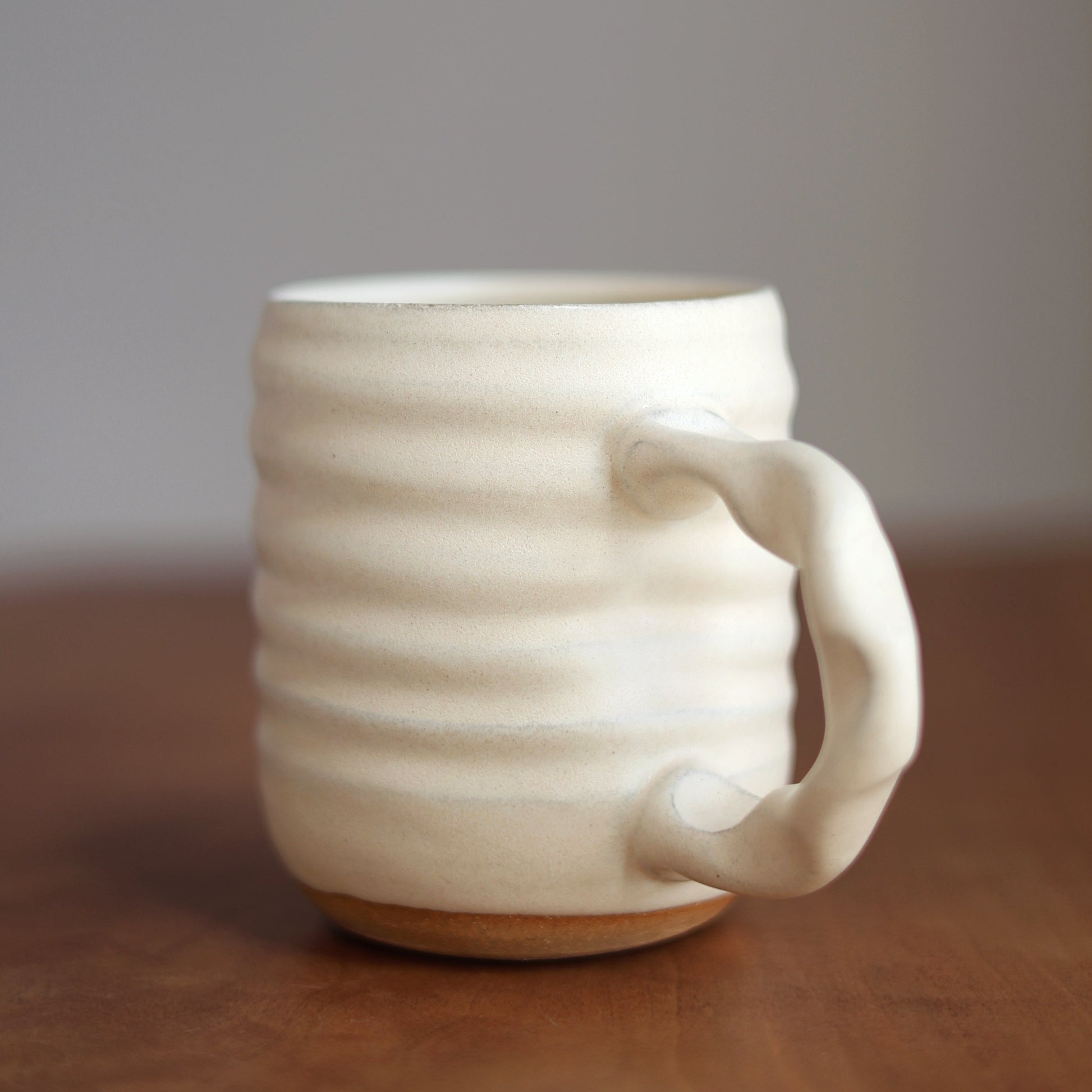 Off White handmade ceramic mug with a handle on a wooden surface and gray background