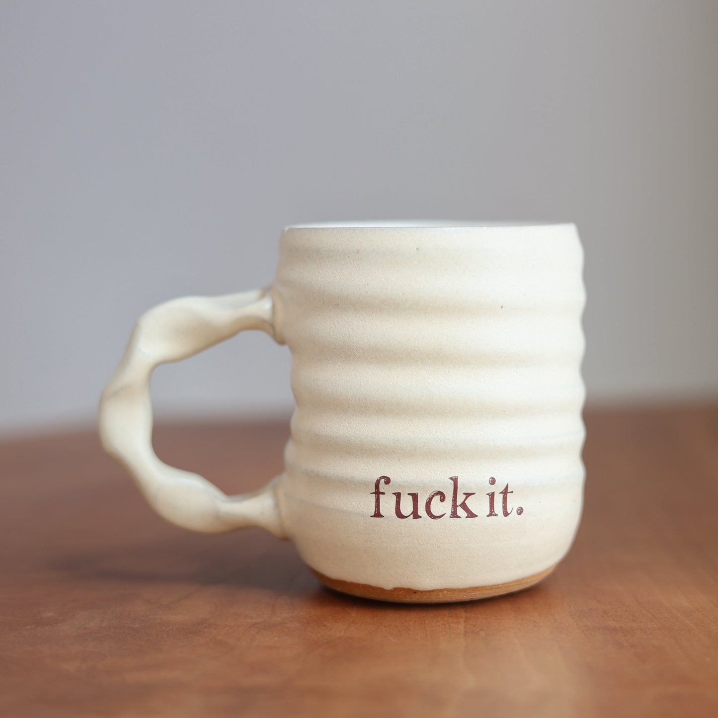 White ceramic mug with 'fuck it.' text on a wooden surface