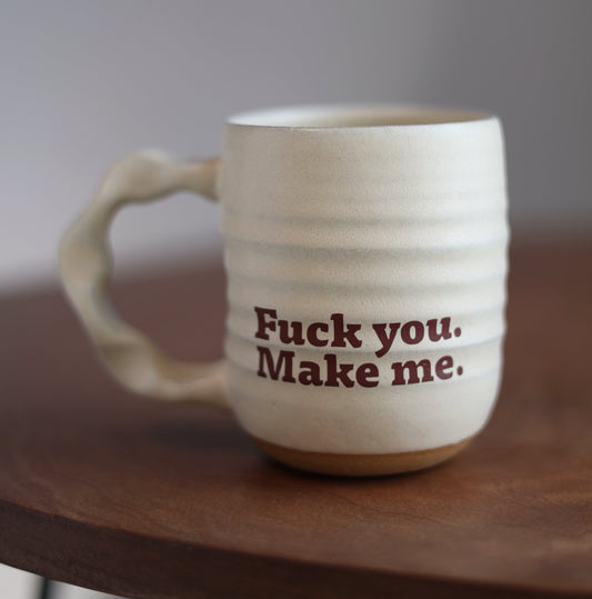 Cream “fuck you make me” ceramic mug with text on a wooden surface