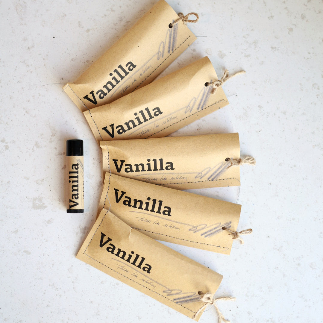 Vanilla-scented lip balms with paper labels on a light surface