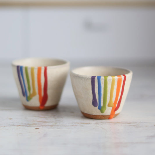 "Small cream ceramic bowl with rainbow drip glaze held in palm of hand, showing colorful striped pattern dripping from rim"