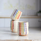 "Cream colored ceramic wine cup featuring rainbow drip glaze pattern with red, orange, yellow, green, blue and purple flowing down the sides"