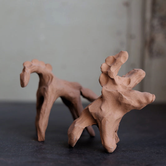 Two clay horse figurines on a dark surface with a neutral background