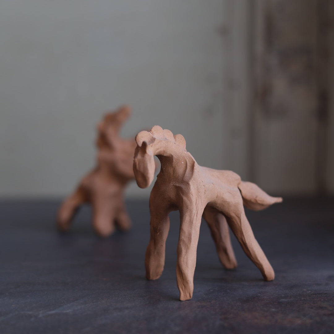 Two small clay figurines of horses on a textured surface with a blurred background.