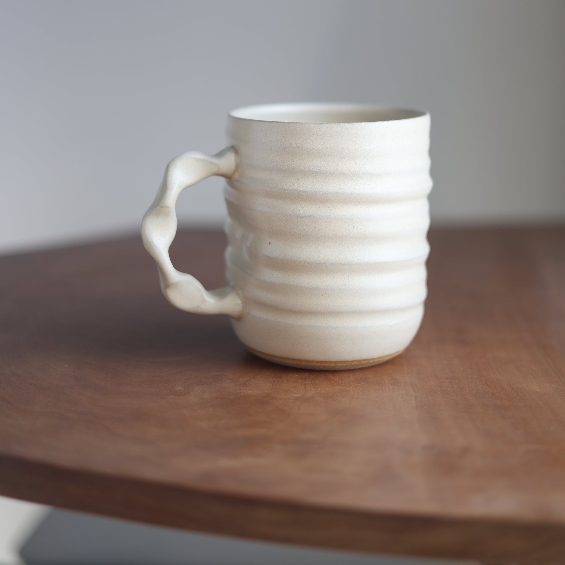 Cream ceramic mug with handle on a wooden surface