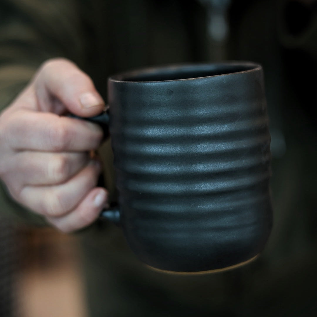Person holding a textured black mug with a blurred background