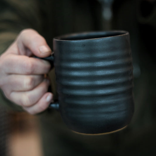 Person holding a textured black mug with a blurred background