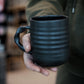 Person holding a black mug with a blurred background
