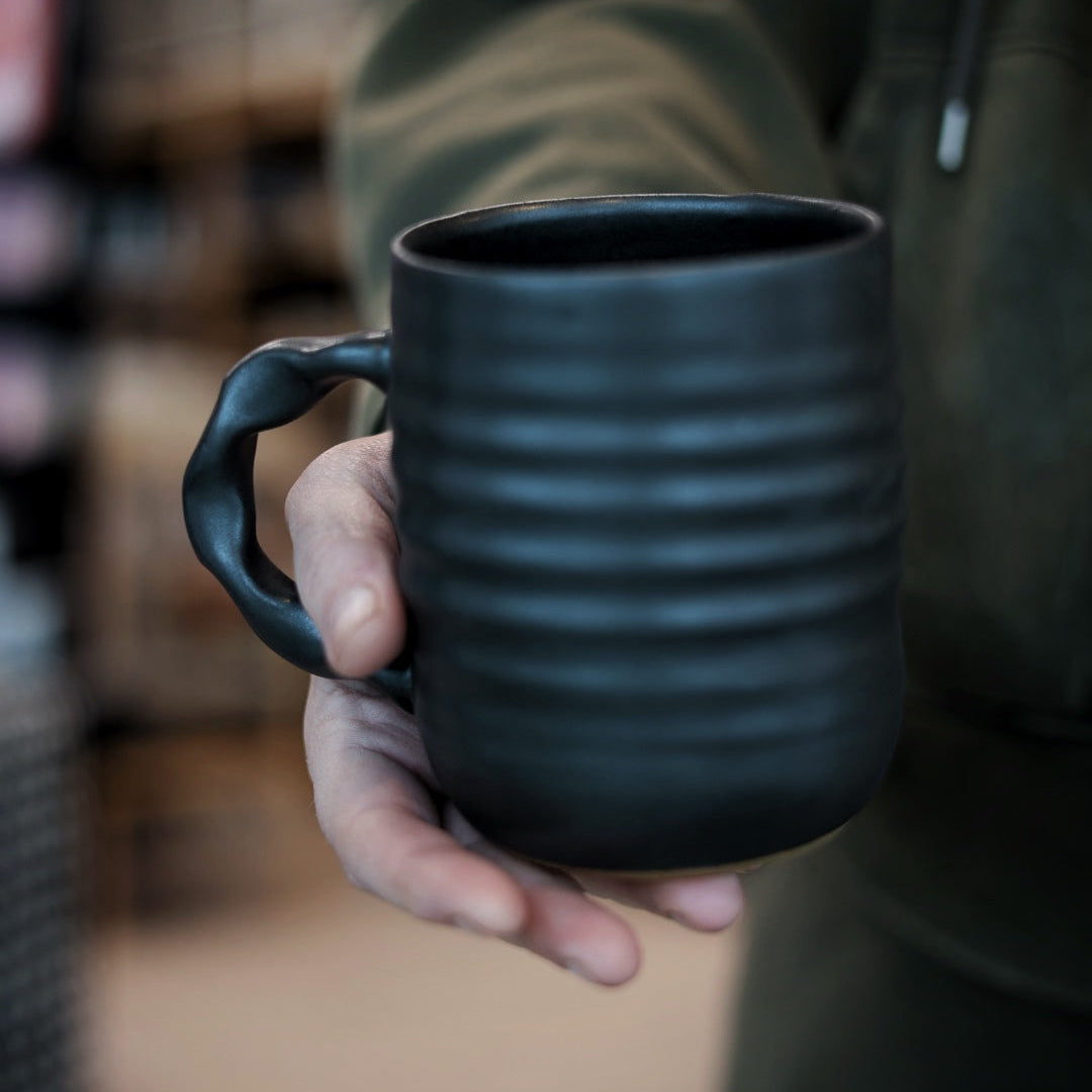 Person holding a black mug with a blurred background