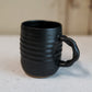 Black ceramic mug with ribbed texture on a light surface