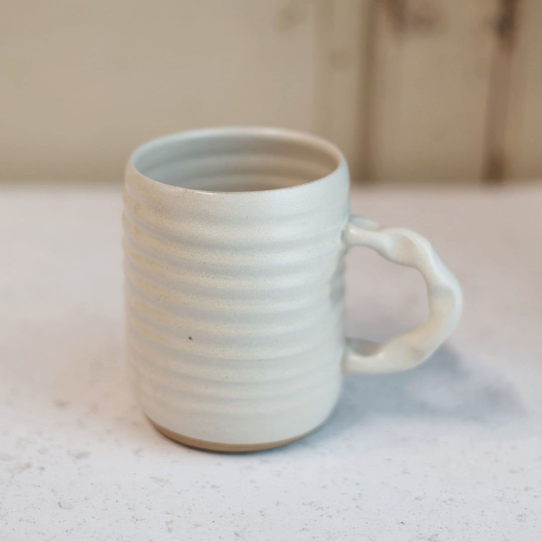Cream ceramic mug on a light surface with a blurred background