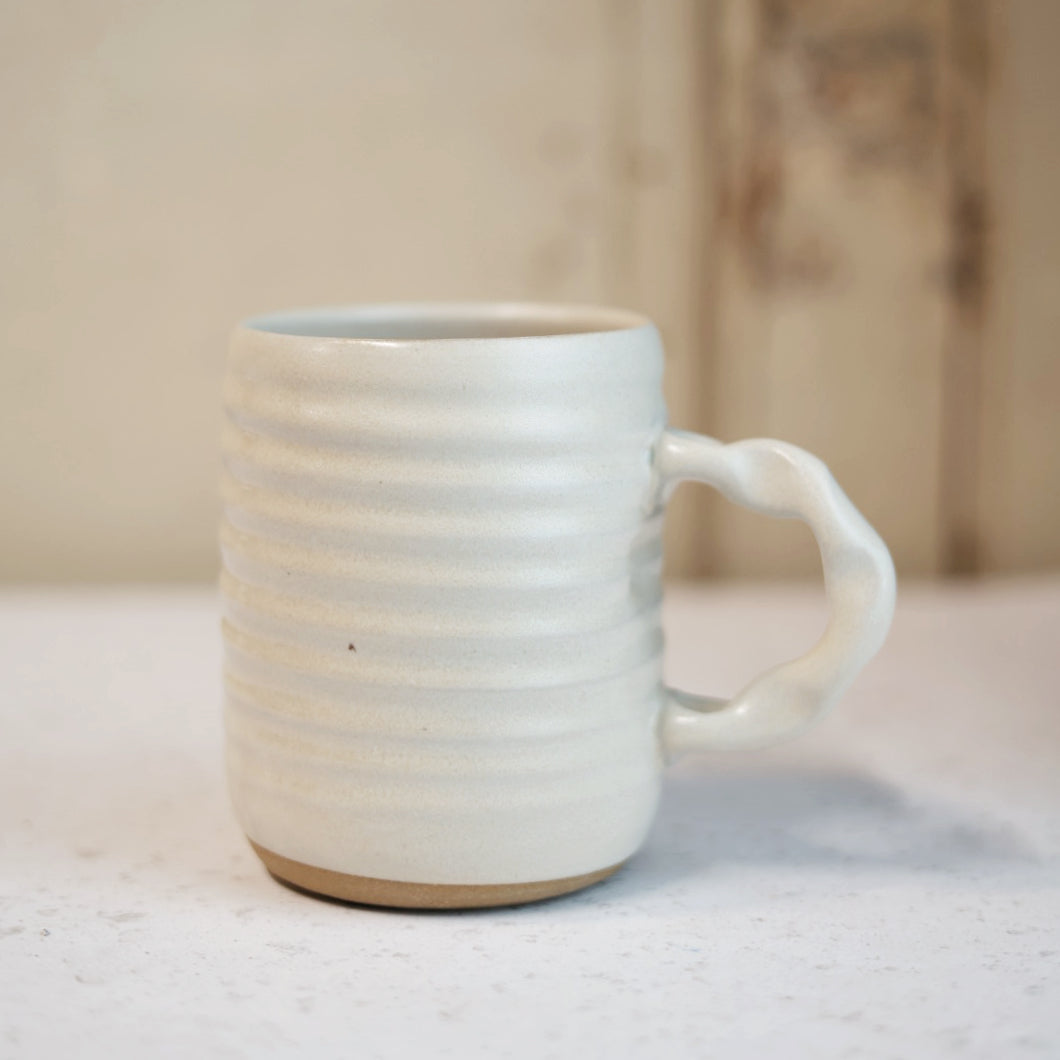 Cream ceramic mug with a handle on a light surface