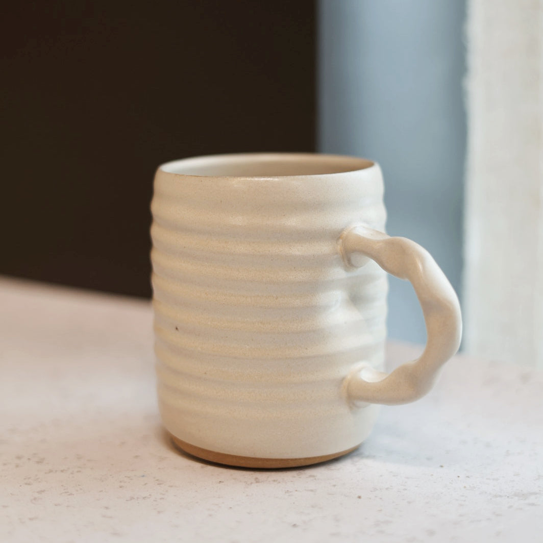 Cream ceramic mug with a handle on a light surface