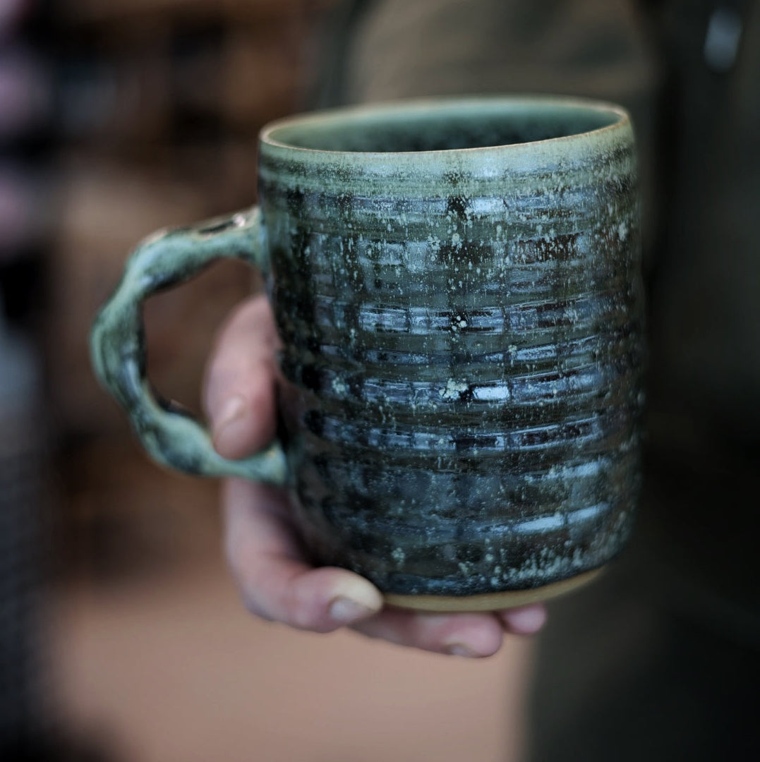 Hand holding a textured ceramic mug with a blurred background