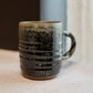 Ceramic mug with green speckled pattern on a neutral background