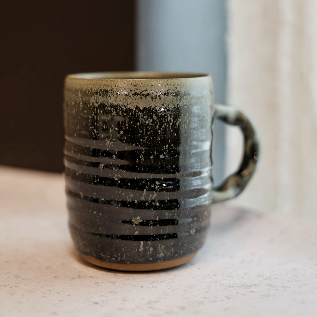 Ceramic mug with green speckled pattern on a neutral background