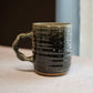 Green ceramic mug with textured surface on a light surface