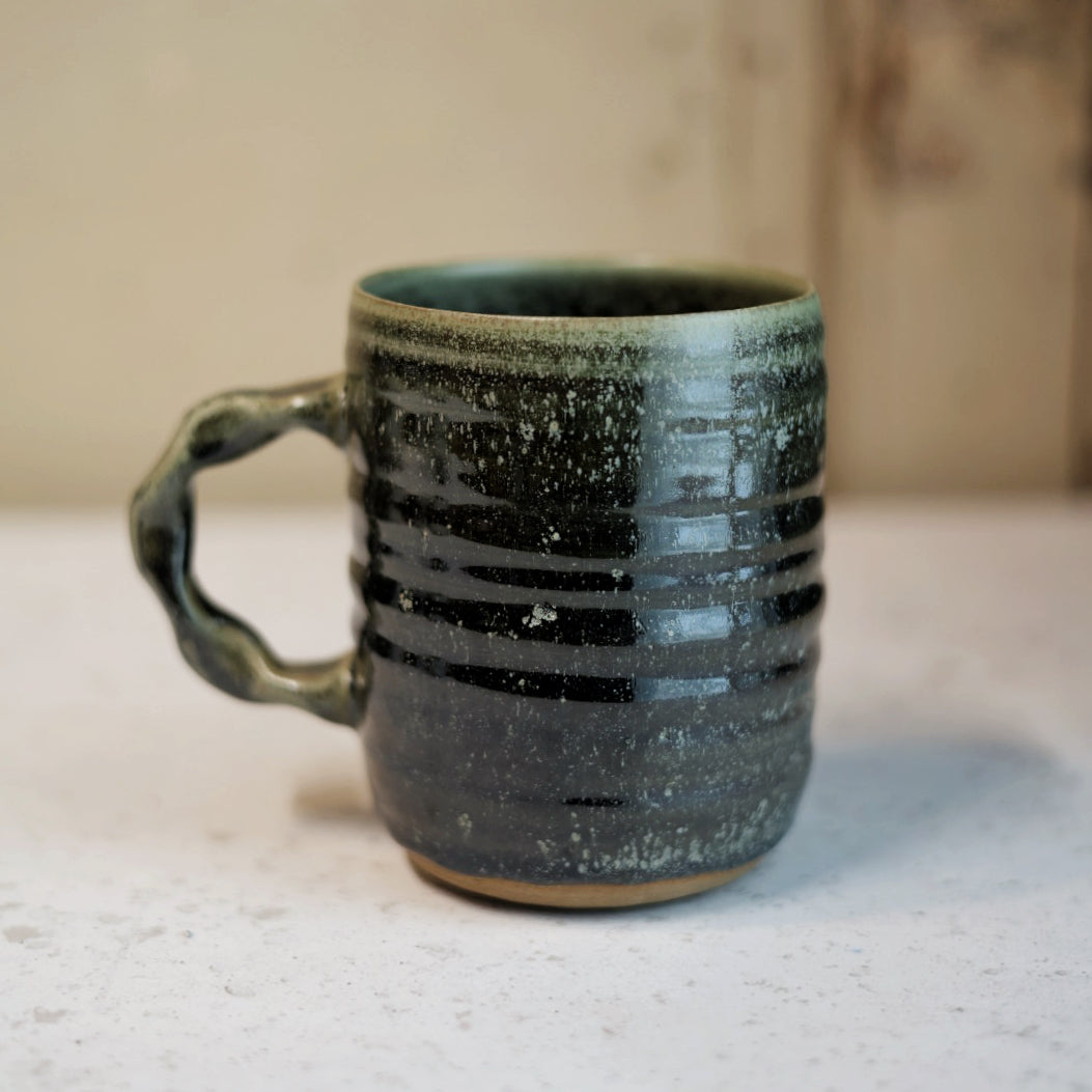 Green speckled ceramic mug on a light surface with a blurred background