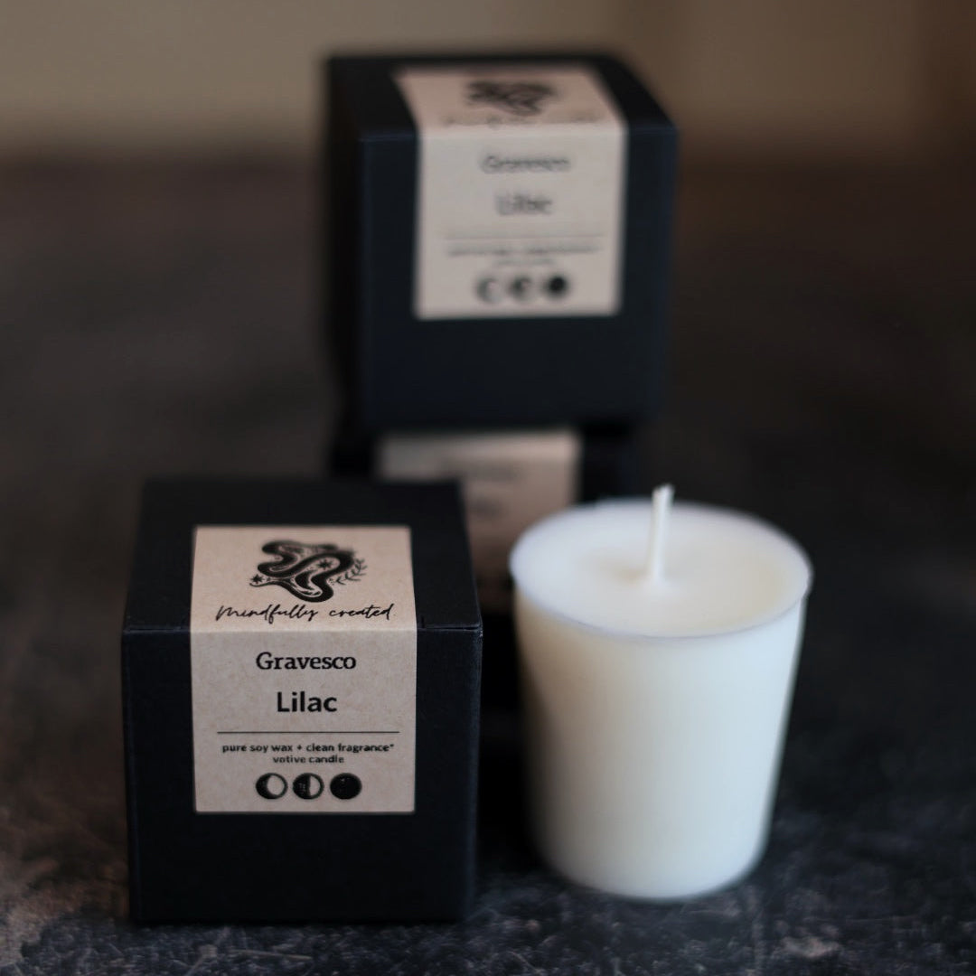 White candle and black boxes labeled 'Gravesco Lilac' on a textured surface.