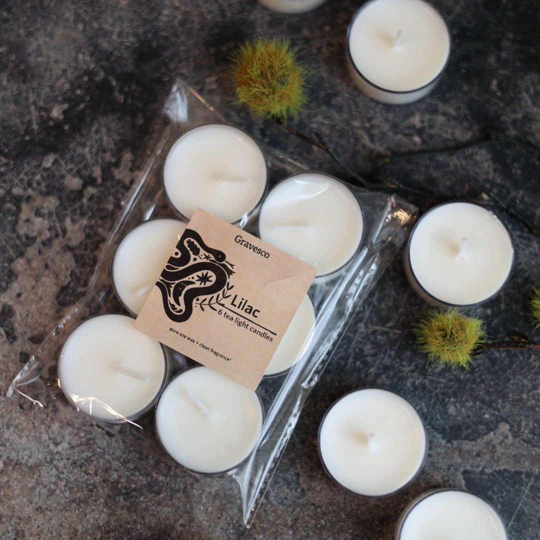 White candles with a visible gravesco Lilac pure soy set of 6 tea light candles  label on a textured surface