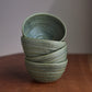 Stack of green ceramic bowls on a wooden surface with a plain background