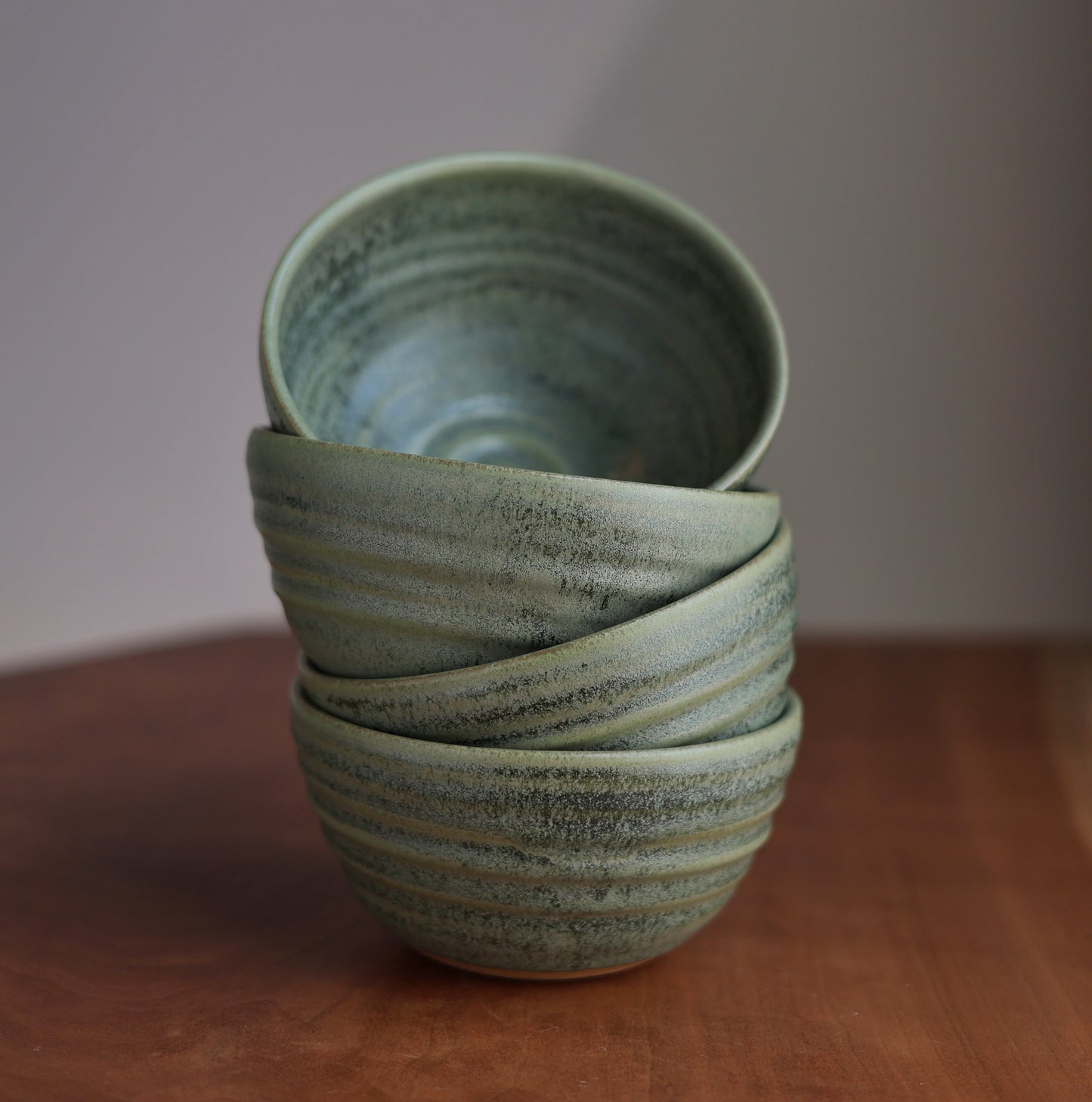 Stack of green ceramic bowls on a wooden surface with a plain background