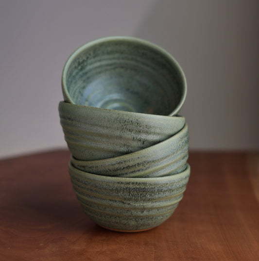 Stack of green ceramic bowls on a wooden surface with a plain background