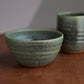 A green ceramic bowl and mug on a wooden surface with a neutral background