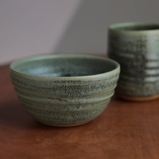 A green ceramic bowl and mug on a wooden surface with a neutral background