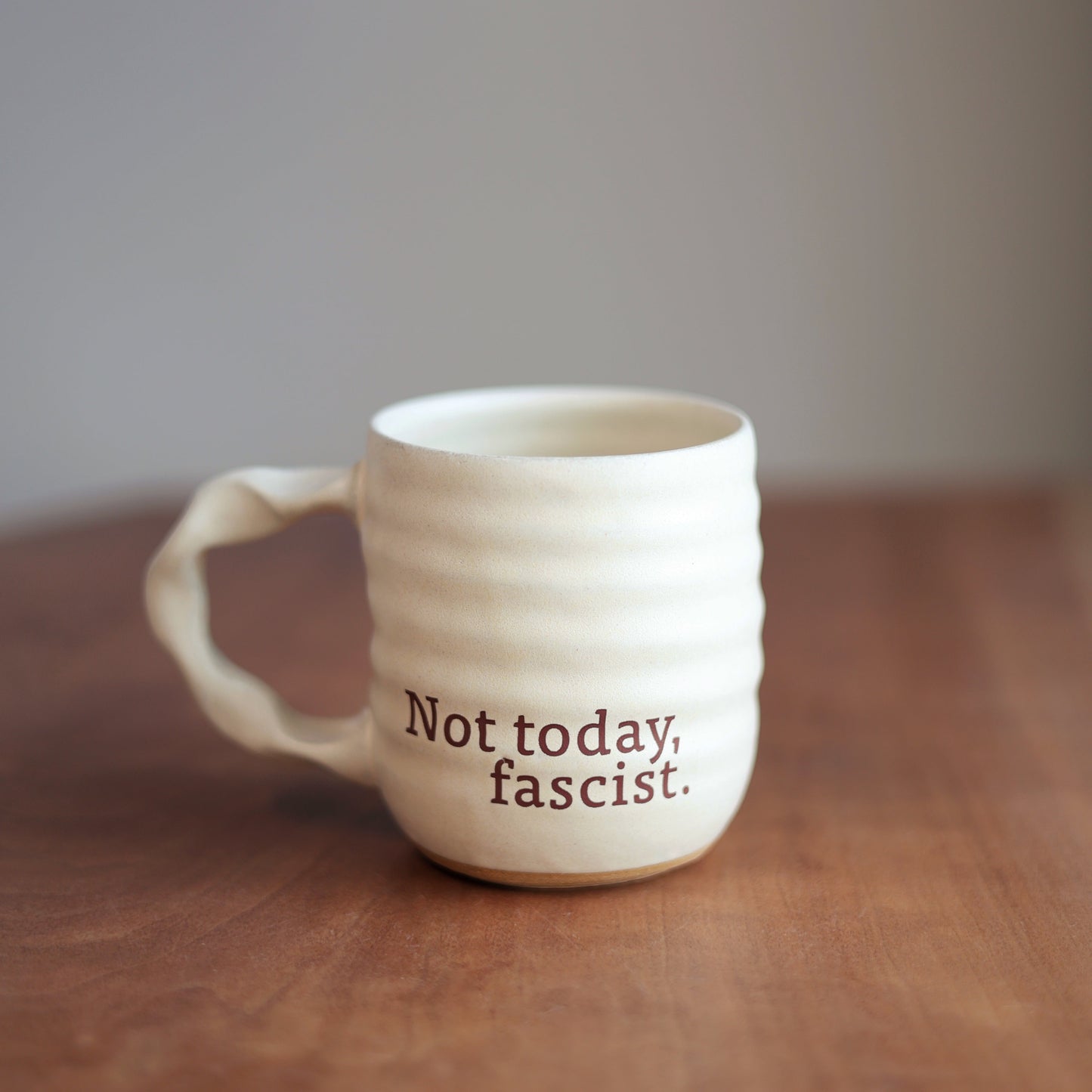 Off White ceramic mug with text 'Not today, fascist.' on a wooden surface.