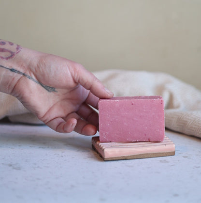 Person holding a small pink bar of soap with a white background