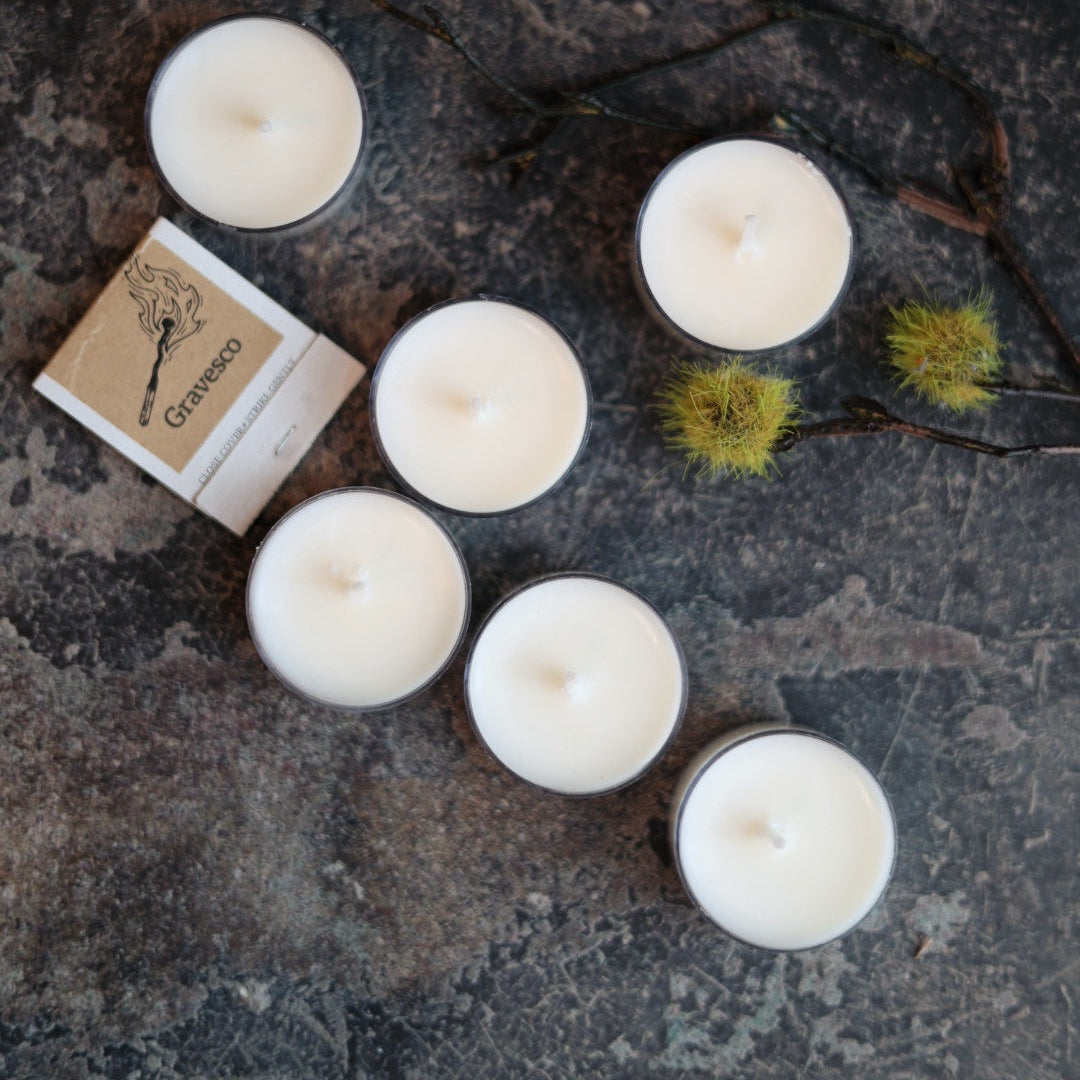 Set of six white candles on a textured surface with a small box labeled 'Candle' in the background.