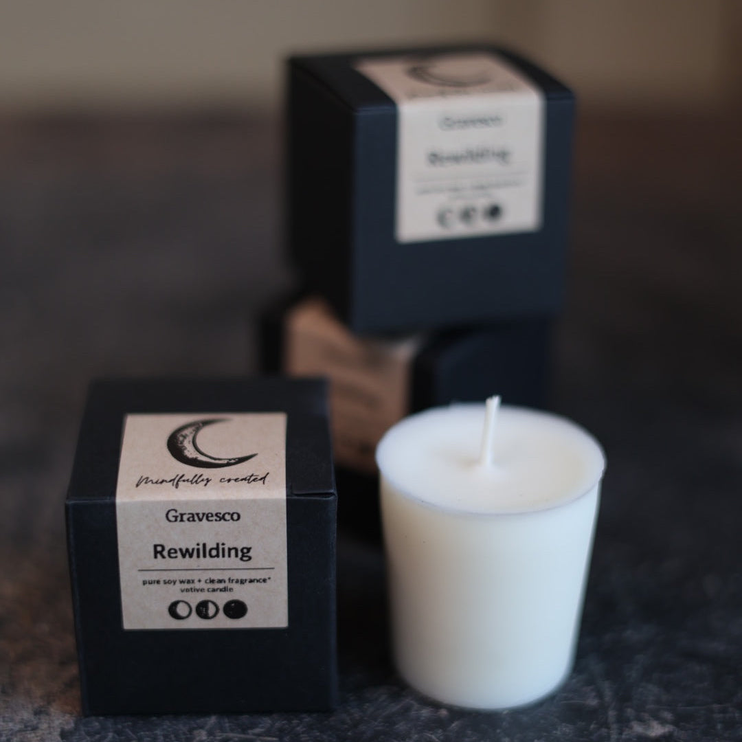 White candle with 'Gravesco Rewilding' packaging on a dark surface