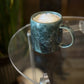 Green handmade ceramic mug with a frothy beverage on a glass table