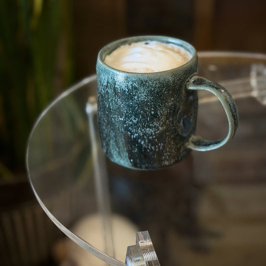 Green handmade ceramic mug with a frothy beverage on a glass table