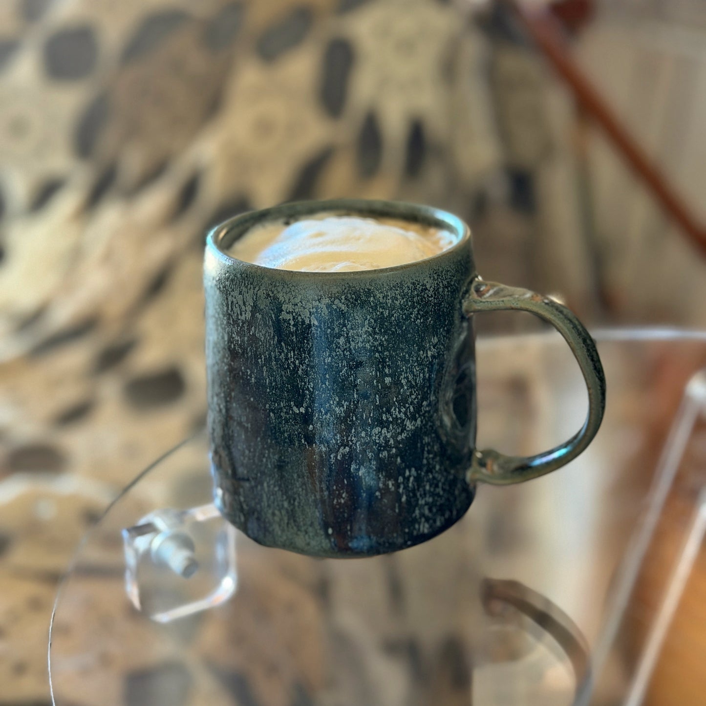 Green speckled mug with a creamy beverage on a glass table