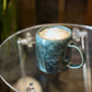 Green ceramic handmade pottery mug with a creamy beverage on a glass table