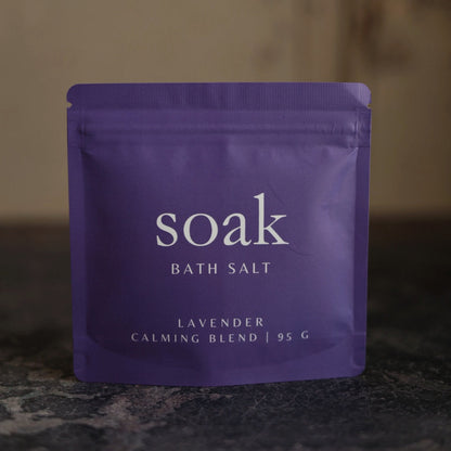 Purple package of 'soak' bath salt on a dark surface with a blurred background