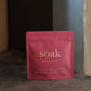 Pink package of 'soak' bath salt on a dark surface with a blurred background